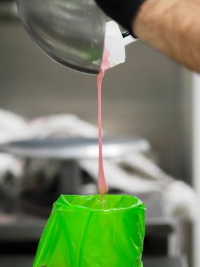 Pasta şefi pipo çantasını dolduruyor. Renk derecelendirme için yenilebilir pembe boyayla karıştırılmış kremalı pasta.