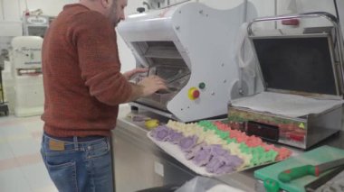 baker slicing red violet yellow and green star cloud and heart shaped coloured buns at catering kitchen for holiday event