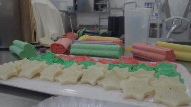 baker slicing red violet yellow and green star cloud and heart shaped coloured buns at catering kitchen for holiday event