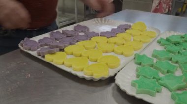 baker slicing red violet yellow and green star cloud and heart shaped coloured buns at catering kitchen for holiday event