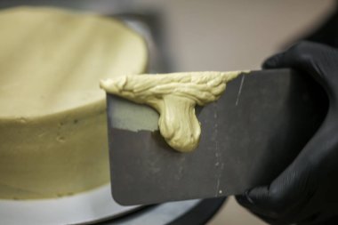 Pasta şefi yeşil şam fıstıklı kremalı pasta yapmak için spatula kazıyıcısı kullanıyor. Düğün pastası hazırlığı.