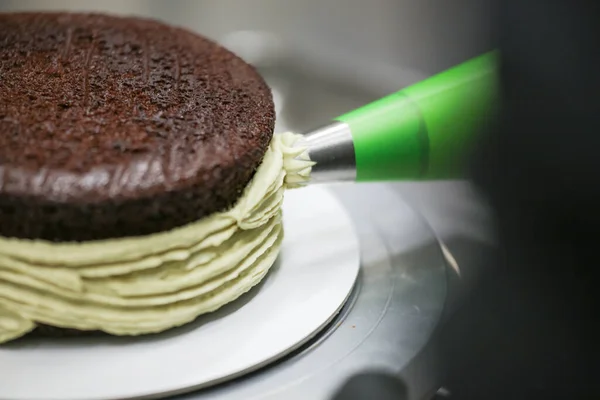 cake chef designer using pistachio cream filling piping bag on layered dark chocolate cake at kitchen lab