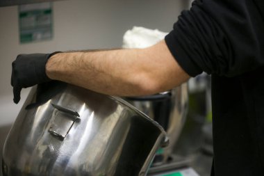 Profesyonel bir mutfakta büyük bir kâseyi yıkayan işçi.