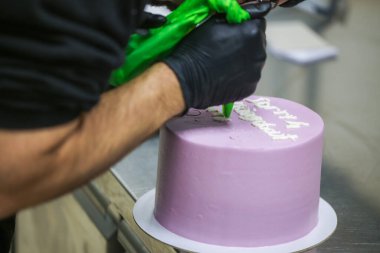 Pasta tasarımcısının üstünde mor kremalı pasta eli beyaz kremayla duygusal pişmanlık mesajı yazıyor.