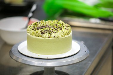 Pasta tasarımcısı yeşil katmanlı çikolatalı kekin üzerine küçük pistacchio ve koyu çikolata parçaları serpiyor.