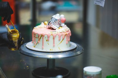 Pasta tasarımcısı kremalı pembe pasta ve el yapımı korunaklı krema üzerine yenilebilir altın boya kullanıyor.