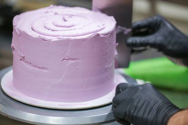 Pasta şefi spatula ve kazıyıcı kullanarak pürüzsüz katmanlı leylak kremalı pasta - düğün pastası hazırlığı