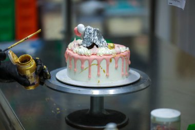 Pasta tasarımcısı kremalı pembe pasta ve el yapımı korunaklı krema üzerine yenilebilir altın boya kullanıyor.