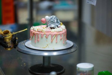 Pasta tasarımcısı kremalı pembe pasta ve el yapımı korunaklı krema üzerine yenilebilir altın boya kullanıyor.