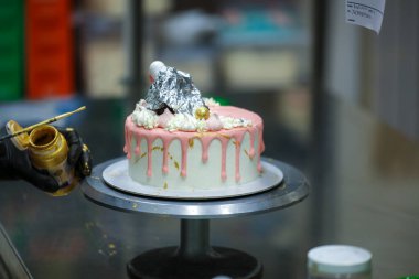 Pasta tasarımcısı kremalı pembe pasta ve el yapımı korunaklı krema üzerine yenilebilir altın boya kullanıyor.