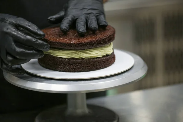 pastry chef designer using pistachio cream and sprinkles on layered dark frosted chocolate cake at kitchen lab