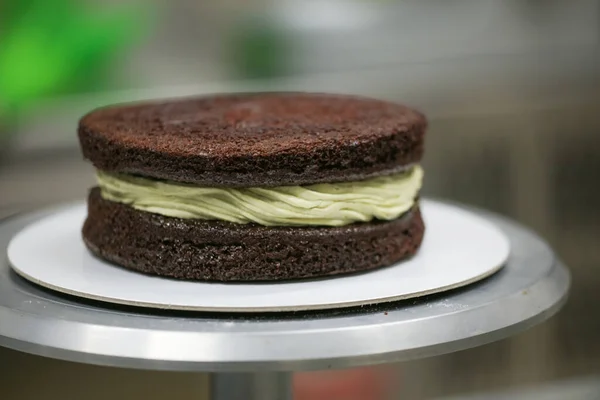 pastry chef designer using pistachio cream and sprinkles on layered dark frosted chocolate cake at kitchen lab