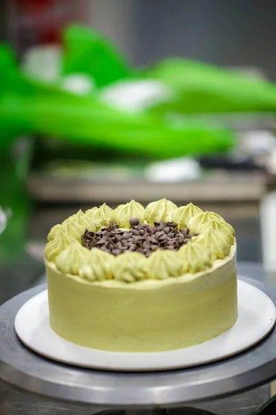 pastry designer sprinkling the top of green layered frosted chocolate cake with small pistacchio and dark chocolate pieces