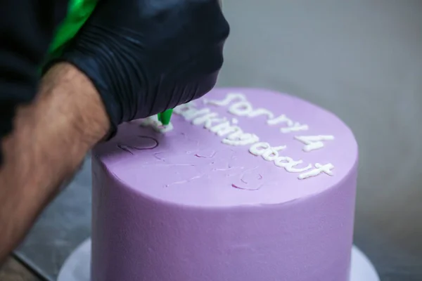 cake designer topping lilac purple frosted cake hand writing emotional regret message with white whipped cream filling