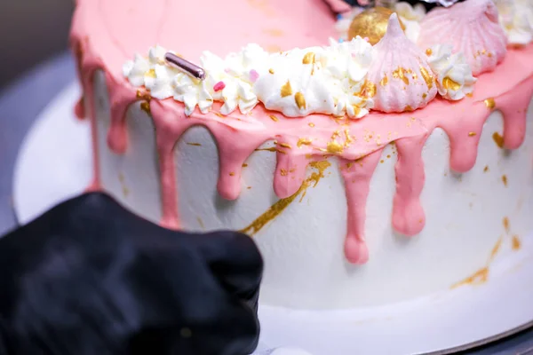 cake designer using edible golden paint on frosted dripping icing pink white cake with protected handmade topping