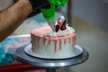 Pasta tasarımcısı pipo torbasını kullanarak kremalı, beyaz, kremalı, el yapımı ve yenilebilir bir oyuncak üzerinde girdaplar yapıyor.