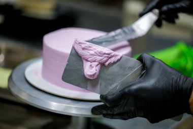 Pasta şefi pürüzsüz leylak pembesi kremalı pasta yapmak için spatula kazıyıcısı kullanıyor. Doğum günü pastası hazırlığı.