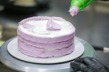Pasta tasarımcısı, mutfak laboratuarında gül kremi dolgu poşeti, katmanlı siyah çikolatalı pasta kullanıyor.