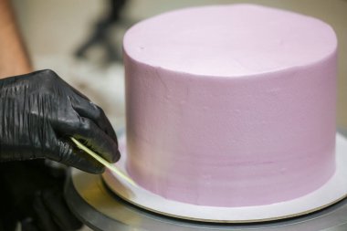 Pasta şefi spatula ve kazıyıcı kullanarak pürüzsüz katmanlı leylak kremalı pasta - düğün pastası hazırlığı