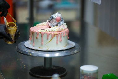 Pasta tasarımcısı kremalı pembe pasta ve el yapımı korunaklı krema üzerine yenilebilir altın boya kullanıyor.