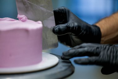 Pasta şefi pürüzsüz leylak pembesi kremalı pasta yapmak için spatula kazıyıcısı kullanıyor. Doğum günü pastası hazırlığı.