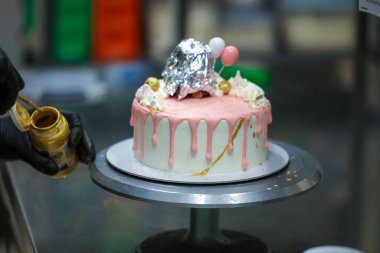 Pasta tasarımcısı kremalı pembe pasta ve el yapımı korunaklı krema üzerine yenilebilir altın boya kullanıyor.