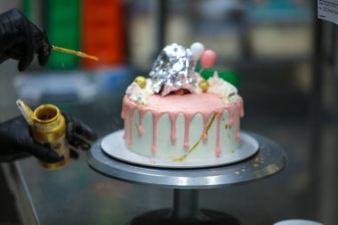 Pasta tasarımcısı kremalı pembe pasta ve el yapımı korunaklı krema üzerine yenilebilir altın boya kullanıyor.