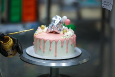 Pasta tasarımcısı kremalı pembe pasta ve el yapımı korunaklı krema üzerine yenilebilir altın boya kullanıyor.