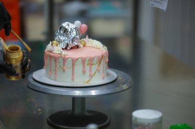 Pasta tasarımcısı kremalı pembe pasta ve el yapımı korunaklı krema üzerine yenilebilir altın boya kullanıyor.