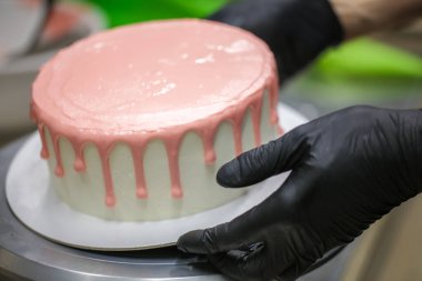 Pasta tasarımcısı, bebek doğum günü kutlaması için beyaz pastaya pembe damlayan bir pasta hazırlıyor.