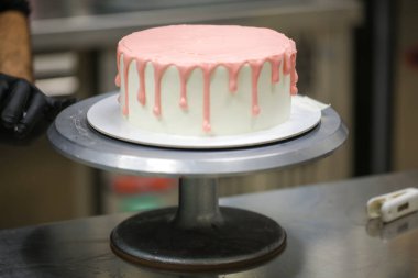 Pasta tasarımcısı, bebek doğum günü kutlaması için beyaz pastaya pembe damlayan bir pasta hazırlıyor.