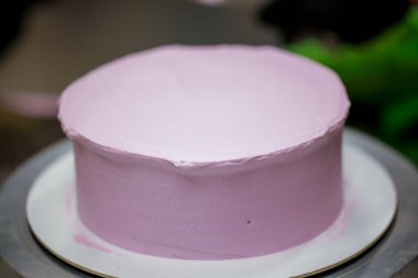 Pasta şefi pürüzsüz leylak pembesi kremalı pasta yapmak için spatula kazıyıcısı kullanıyor. Doğum günü pastası hazırlığı.