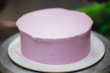 Pasta şefi pürüzsüz leylak pembesi kremalı pasta yapmak için spatula kazıyıcısı kullanıyor. Doğum günü pastası hazırlığı.