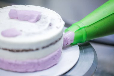 Pasta tasarımcısı, mutfak laboratuarında gül kremi dolgu poşeti, katmanlı siyah çikolatalı pasta kullanıyor.