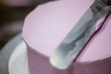 Pasta şefi pürüzsüz leylak pembesi kremalı pasta yapmak için spatula kazıyıcısı kullanıyor. Doğum günü pastası hazırlığı.