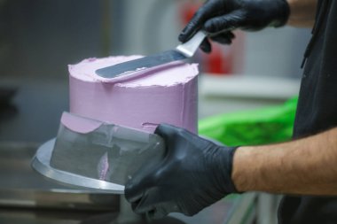 Pasta şefi spatula ve kazıyıcı kullanarak pürüzsüz katmanlı leylak kremalı pasta - düğün pastası hazırlığı