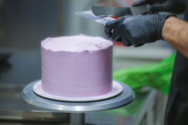 Pasta şefi spatula ve kazıyıcı kullanarak pürüzsüz katmanlı leylak kremalı pasta - düğün pastası hazırlığı