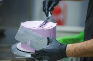 Pasta şefi spatula ve kazıyıcı kullanarak pürüzsüz katmanlı leylak kremalı pasta - düğün pastası hazırlığı