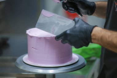 Pasta şefi spatula ve kazıyıcı kullanarak pürüzsüz katmanlı leylak kremalı pasta - düğün pastası hazırlığı