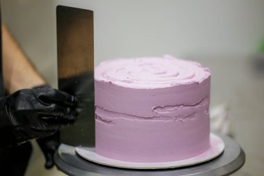 Pasta şefi spatula ve kazıyıcı kullanarak pürüzsüz katmanlı leylak kremalı pasta - düğün pastası hazırlığı