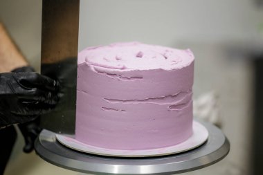 Pasta şefi spatula ve kazıyıcı kullanarak pürüzsüz katmanlı leylak kremalı pasta - düğün pastası hazırlığı