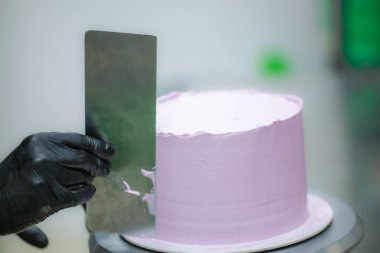 Pasta şefi spatula ve kazıyıcı kullanarak pürüzsüz katmanlı leylak kremalı pasta - düğün pastası hazırlığı