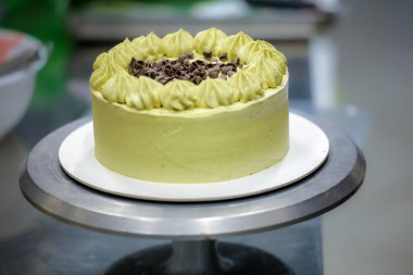 Pasta tasarımcısı yeşil katmanlı çikolatalı kekin üzerine küçük pistacchio ve koyu çikolata parçaları serpiyor.