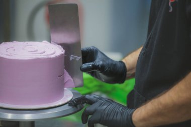 Pasta şefi spatula ve kazıyıcı kullanarak pürüzsüz katmanlı leylak kremalı pasta - düğün pastası hazırlığı