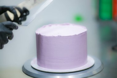 Pasta şefi spatula ve kazıyıcı kullanarak pürüzsüz katmanlı leylak kremalı pasta - düğün pastası hazırlığı