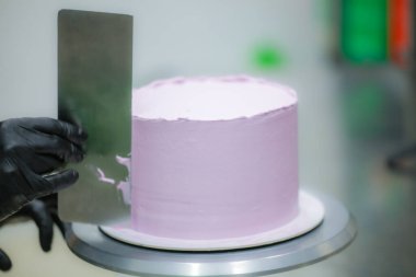 Pasta şefi spatula ve kazıyıcı kullanarak pürüzsüz katmanlı leylak kremalı pasta - düğün pastası hazırlığı