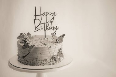 Donmuş leylak kremalı pasta üzerinde doğum günü tabelası ve beyaz arka planda duran kelebekler - siyah ve mor tatlı yiyecekler renklendiriyor