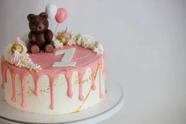 stock image frosted dripping icing pink white cake with handmade bear topping on stand on white background for one year old baby girl