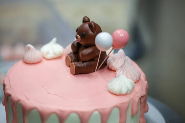 cake designer finishing decoration on frosted dripping icing pink white cake handmade bear edible topping