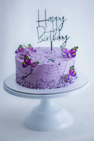 frosted layered icing lilac cake with happy birthday sign and butterflies topper on stand on white background - black and purple sweet food colorizing